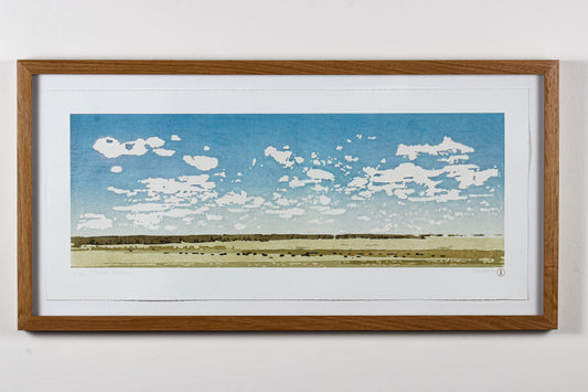 Framed wood print of a landscape with blue sky and white clouds