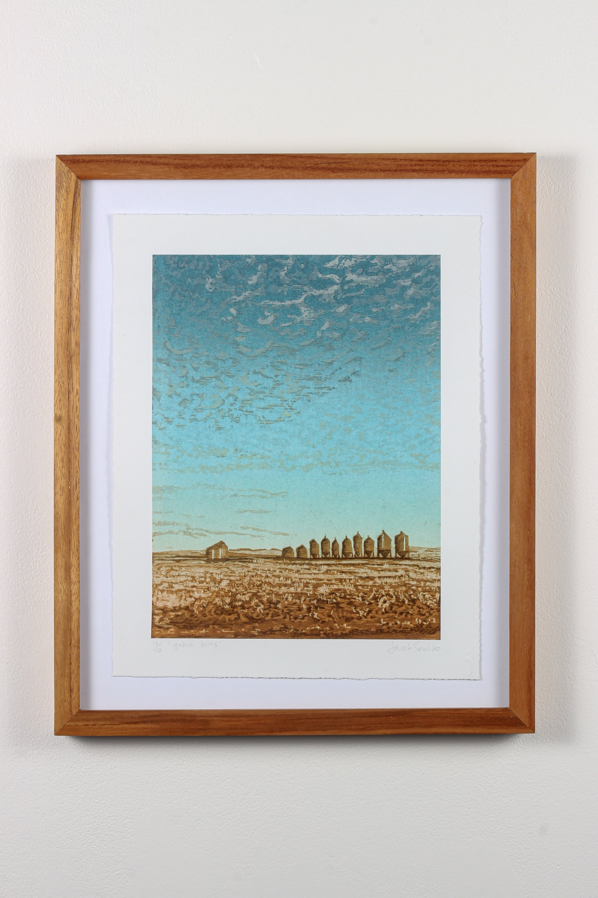 Framed wood print of blue sky, small clouds, and a field with grain bins in Saskatchewan.