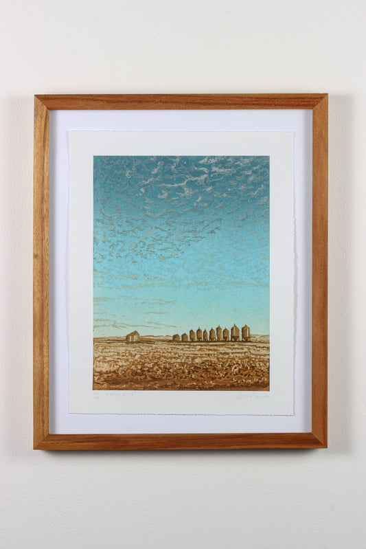 Framed wood print of blue sky, small clouds, and a field with grain bins in Saskatchewan.