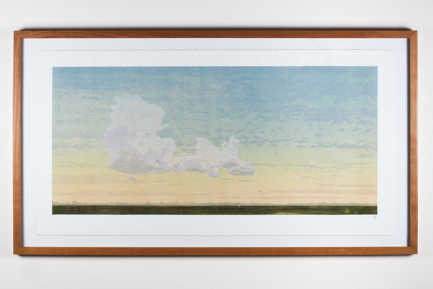 Framed wood cut print of a large cloud in a blue and yellow sky over a dark green field.