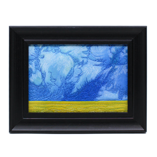 Thread painting of a large blue sky over a canola field