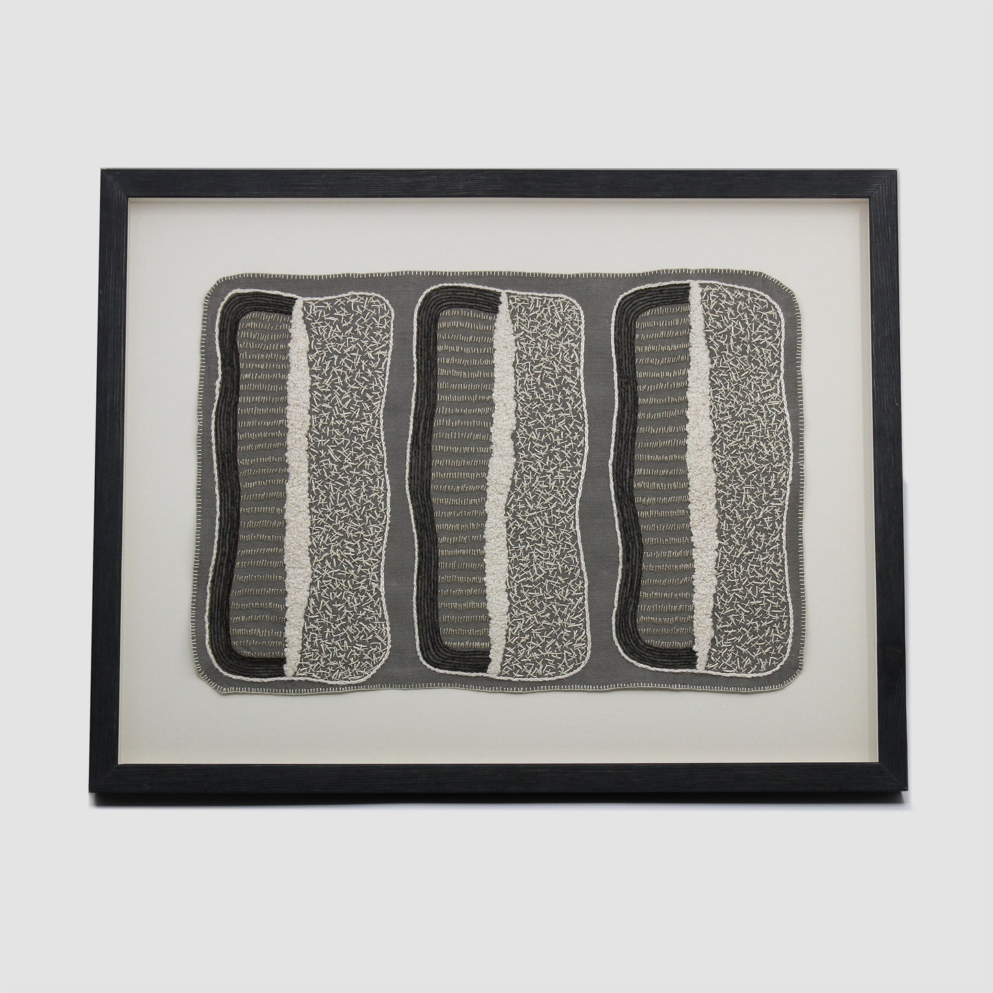 Framed embroidery of three black and white rectangles embroidered on grey cloth