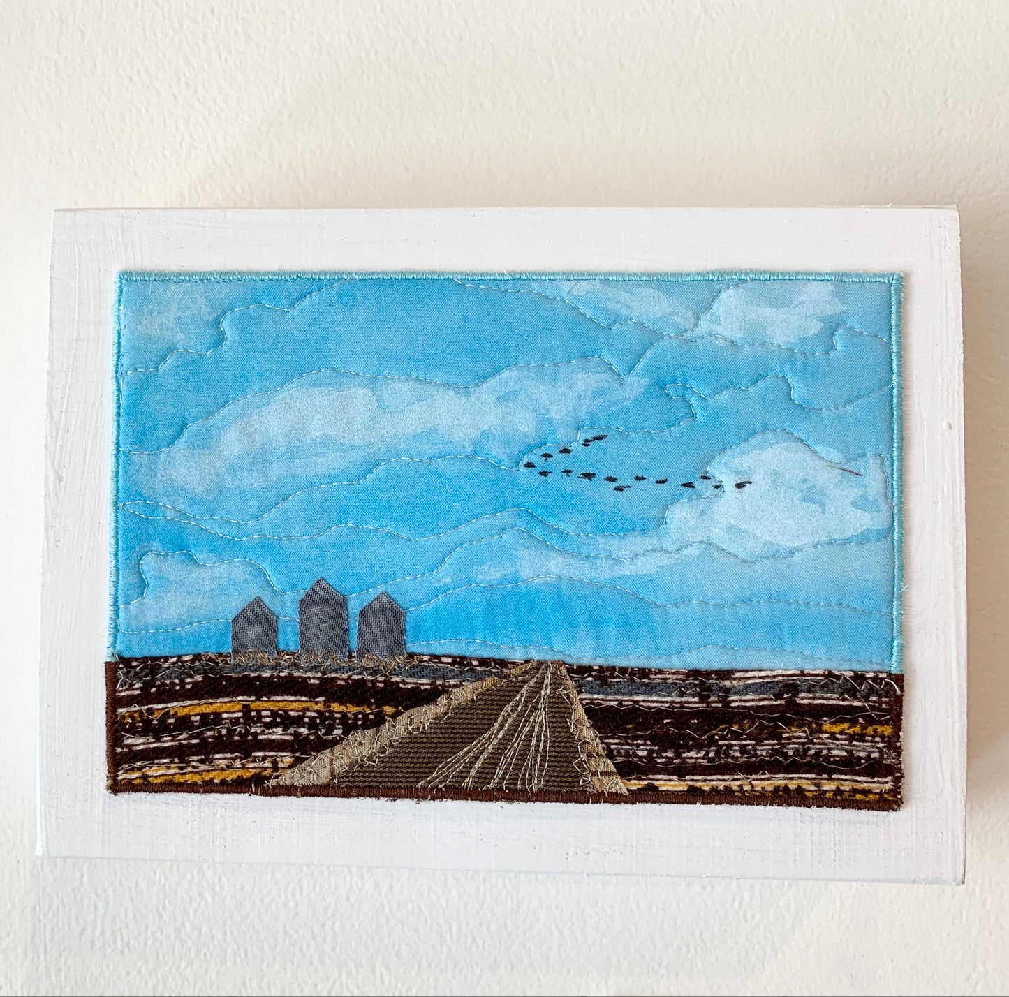 Blue and brown fibre art of Saskatchewan landscape on a white wood block