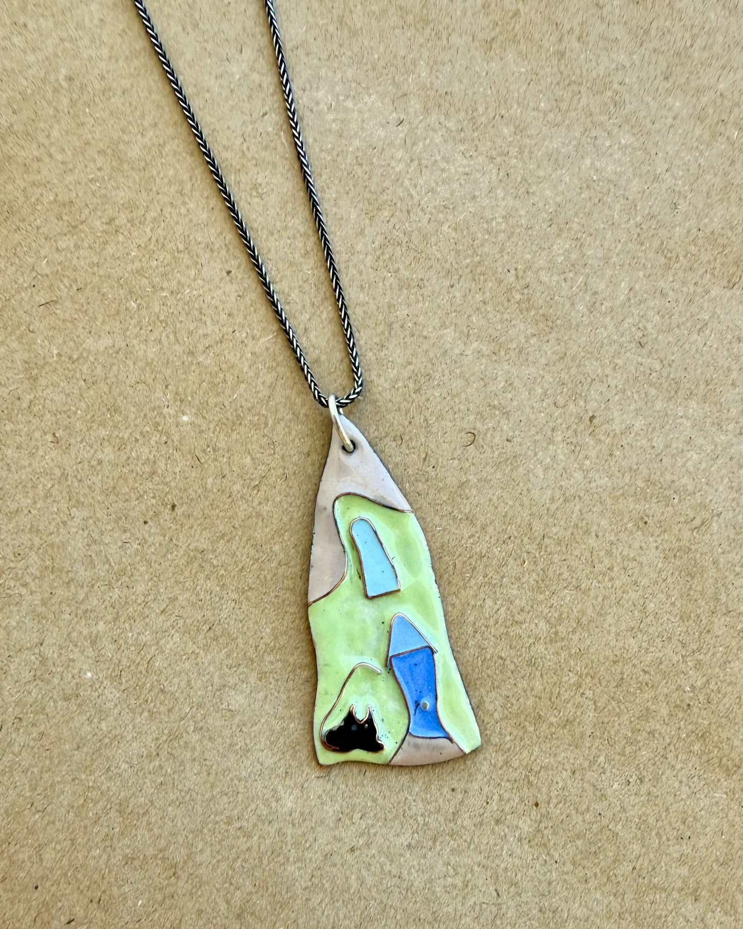 Necklace with a unique pendant on a beige background. The pendant is in the shape of a green house with a blue door and a black cat peeking through the front window.