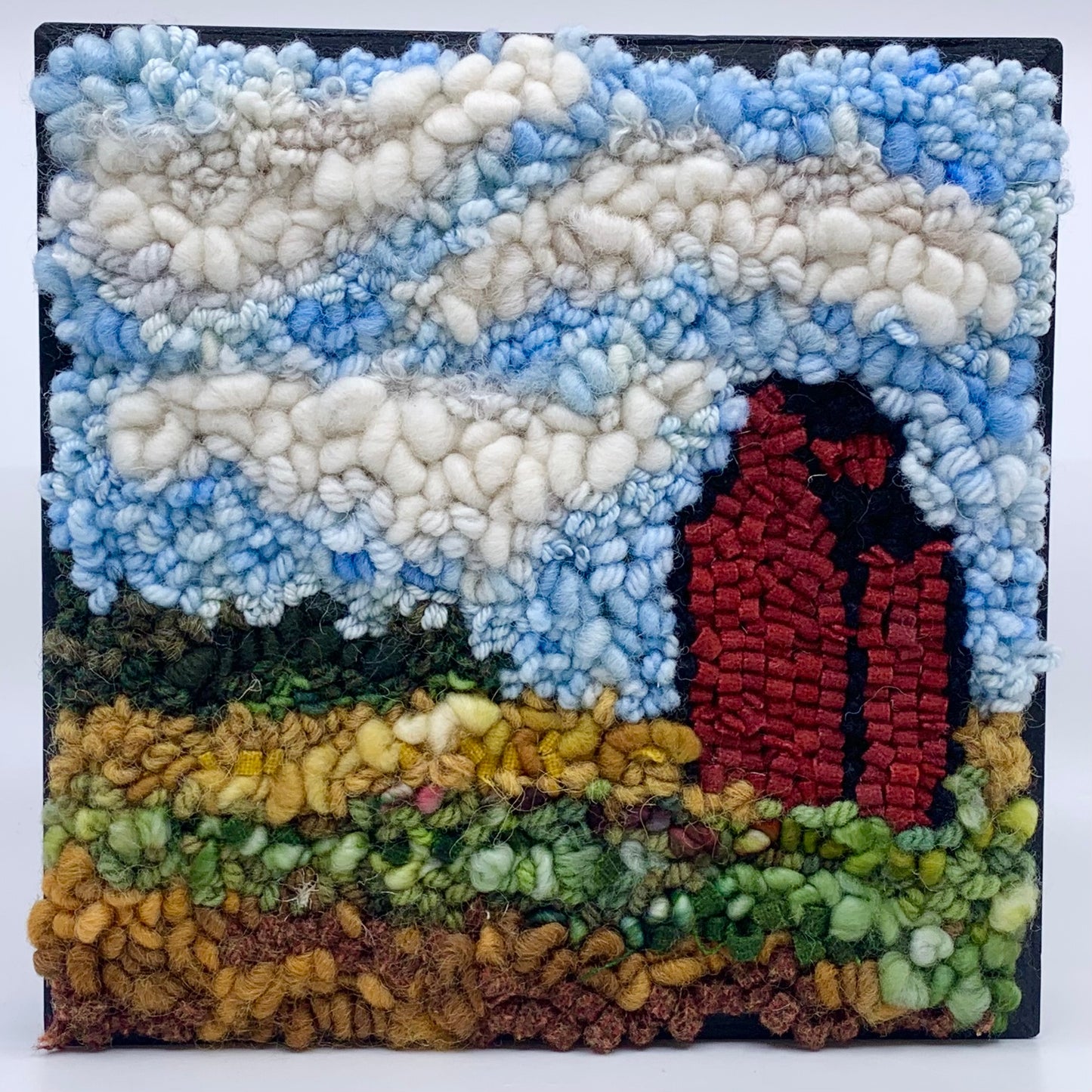 Rug hooked landscape of a red grain elevator and blue sky