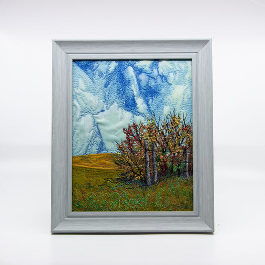 Embroidered scene of a prairie field, fence, and sky. 