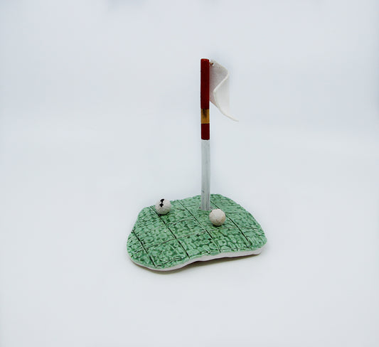 Clay golf green with red flag and two golf balls