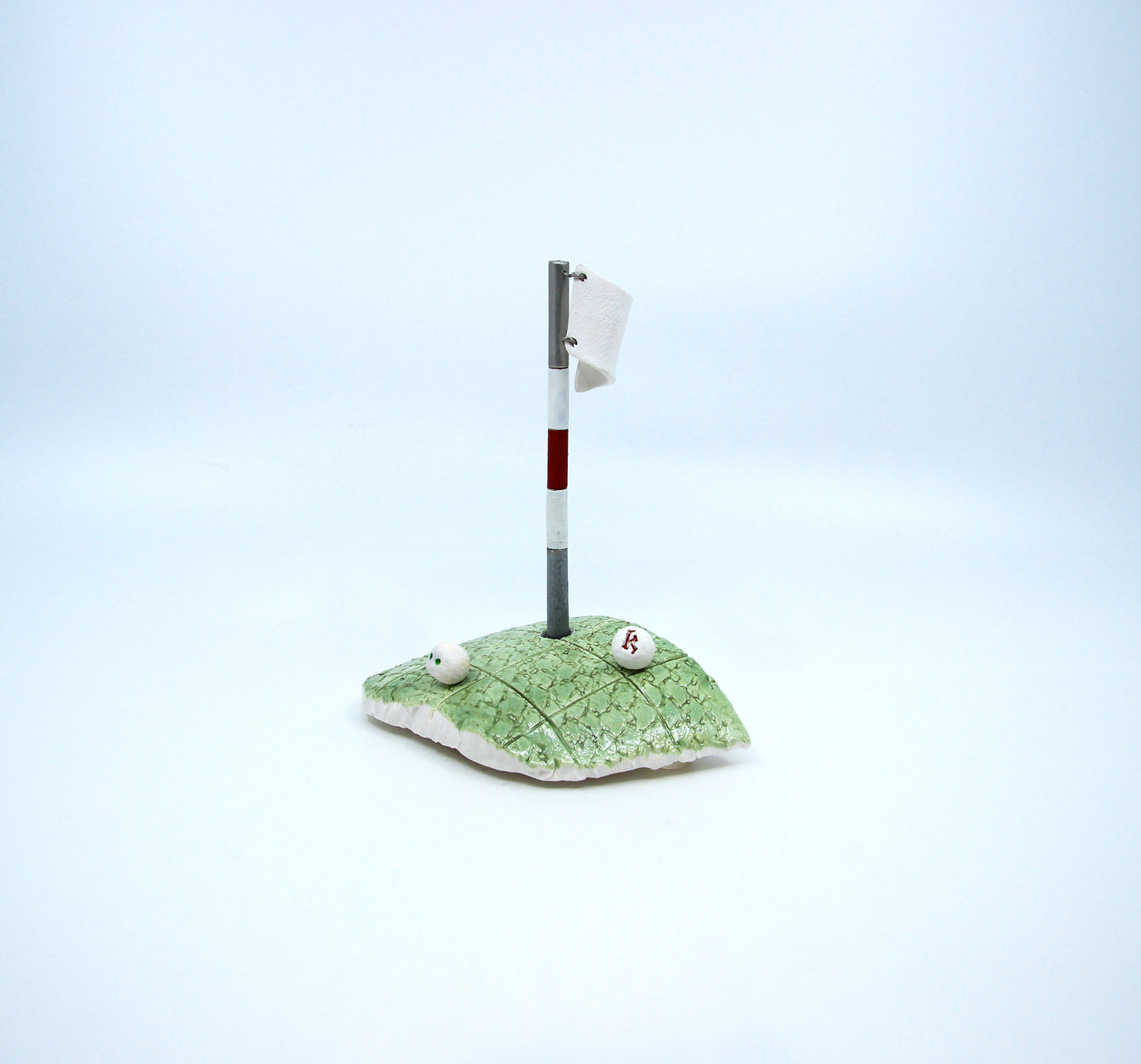 Clay golf green with white golf flag and two golf balls