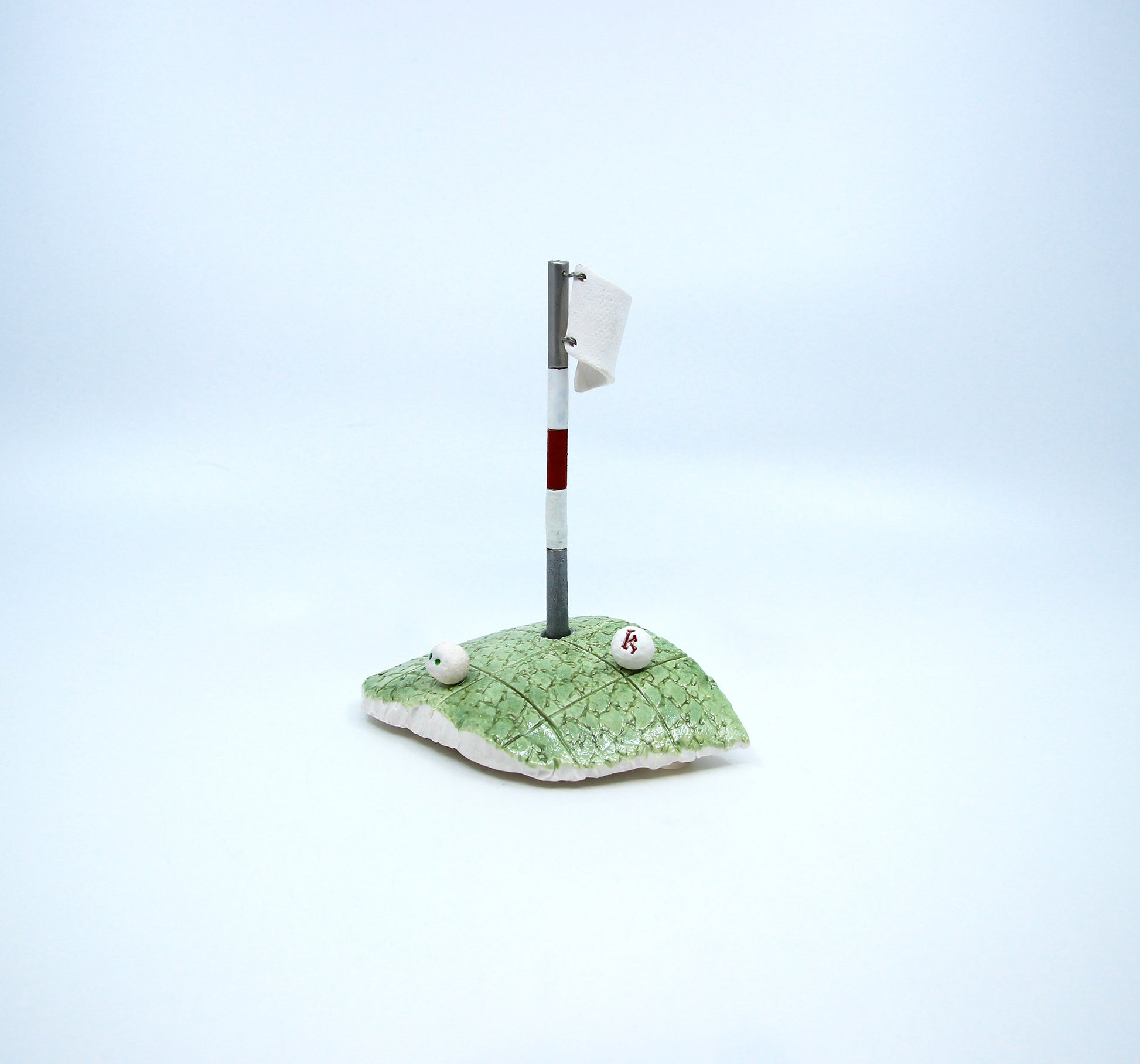 Clay golf green with white golf flag and two golf balls