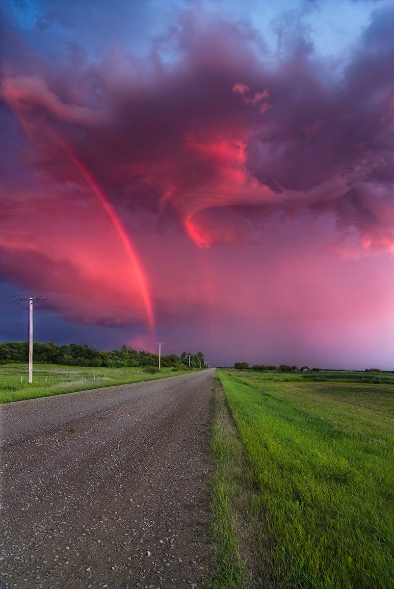 Photograph of a pink and purple sky with a rainbow and a road