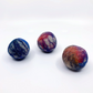 Three hand-felted wool balls in marbled colors of blue, purple, red, and white, arranged on a plain white background.