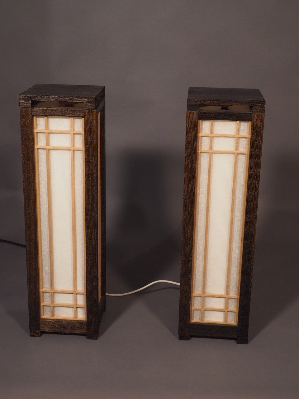 Two wooden lamps with glass panels on a gray background
