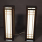 Two wooden lamps with glass panels on a dark background