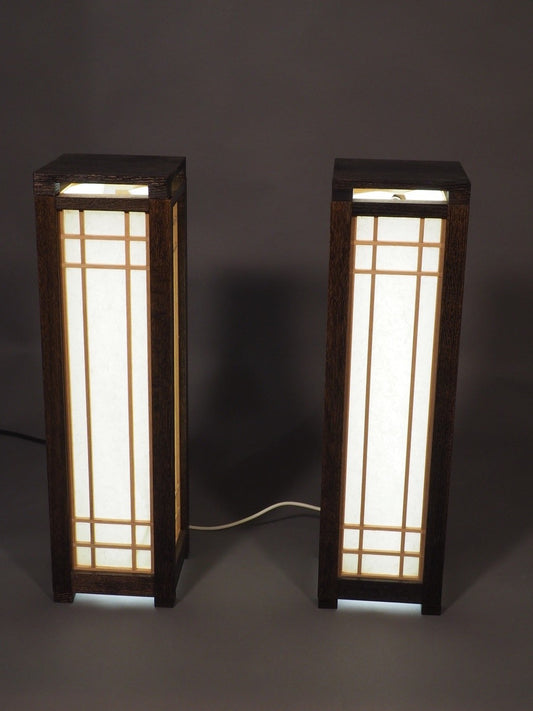 Two wooden lamps with glass panels on a dark background