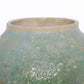 Close up shot of a round ceramic vessel. The mouth is smooth and symmetrical, with bubbly green glaze on the outside.