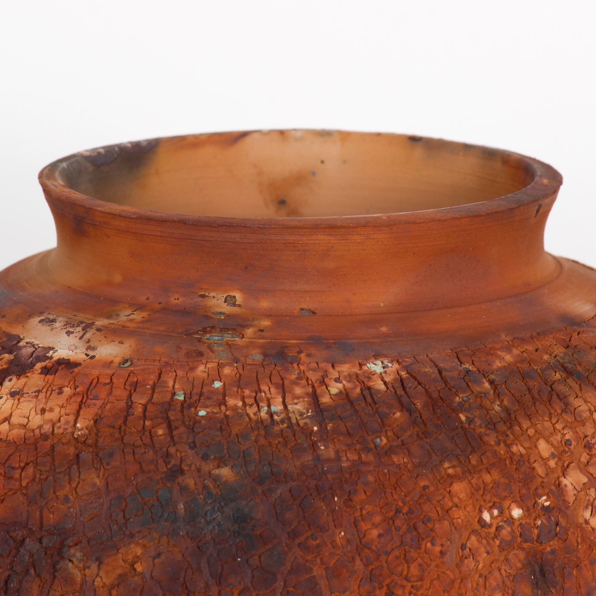 A round ceramic vessel. Surface is textured, with rust brown and orange crackly splotches.