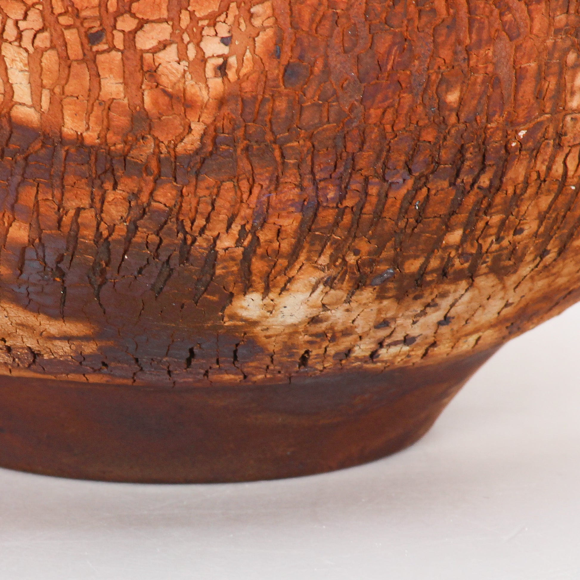 A round ceramic vessel. Surface is textured, with rust brown and orange crackly splotches.