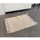 Pink and Green woven rug with fringe laying in front of a cabinet