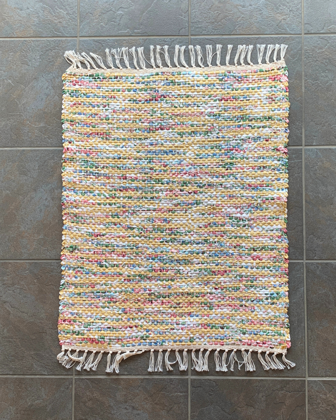 top down view of a colourful woven rug with fringe laying flat on the ground