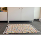 Colourful woven rug with fringe laying in front of a cabinet 