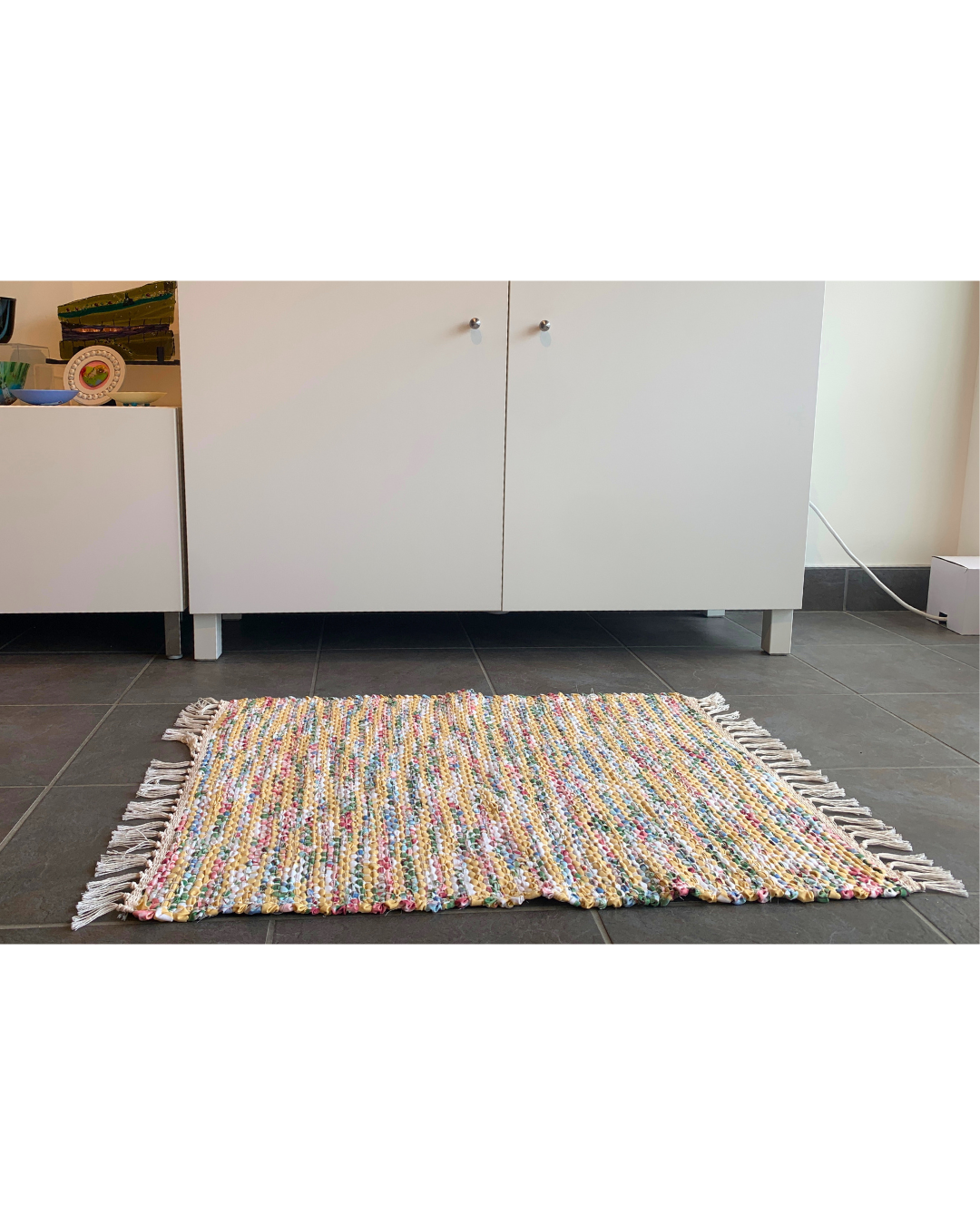 Colourful woven rug with fringe laying in front of a cabinet 