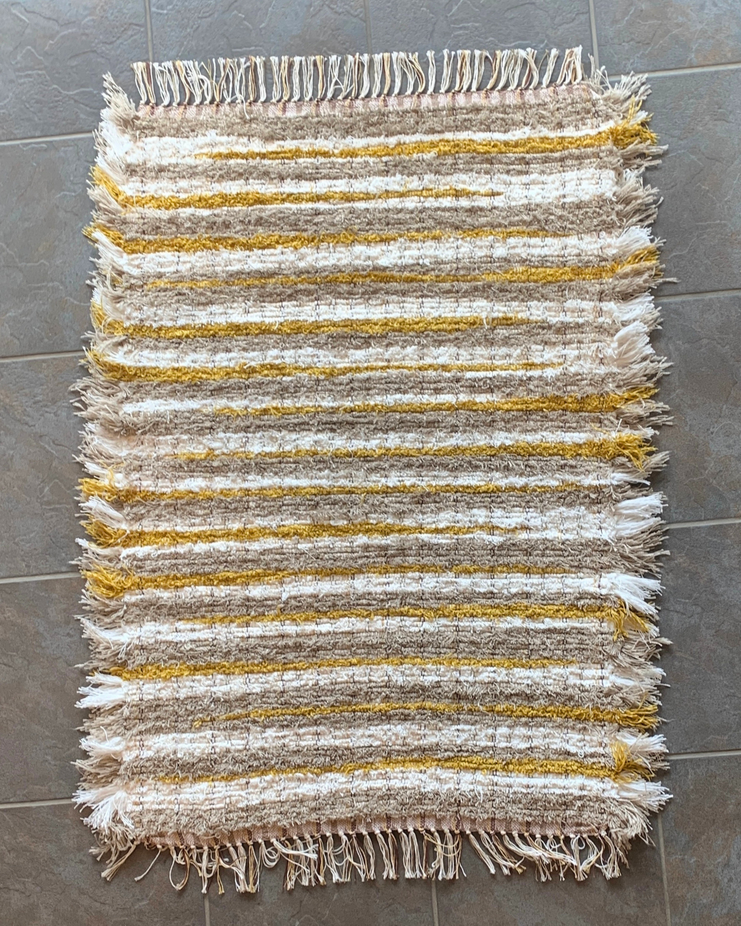 A top down view of a Brown, white and mustard woven fringe rug laying on the floor