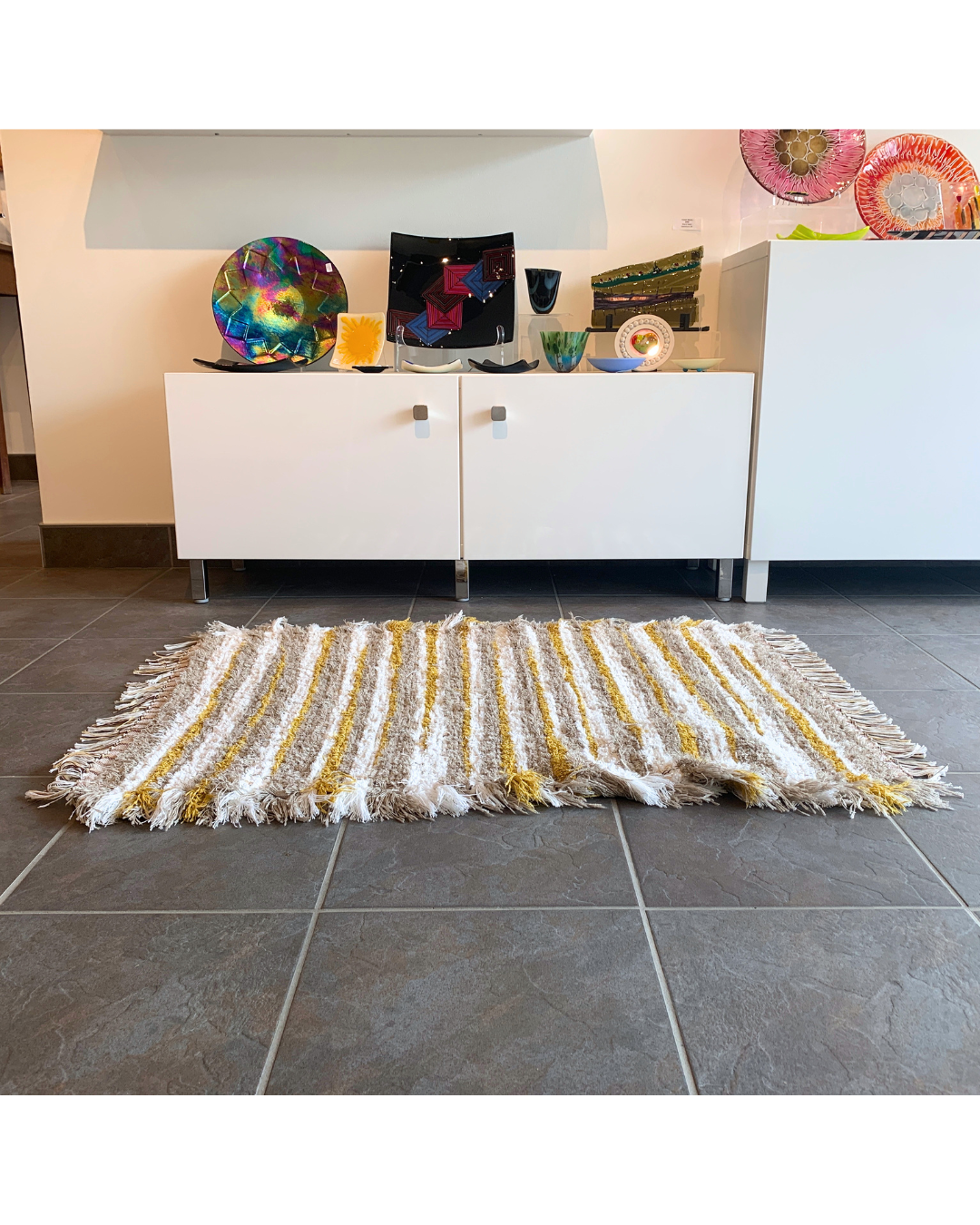 A Brown, white and mustard woven fringe rug laying in front of a cabinet
