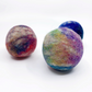 Three hand-felted wool balls in marbled, tie-dye-like colors, including purple, blue, green, yellow, and pink, arranged on a white background.