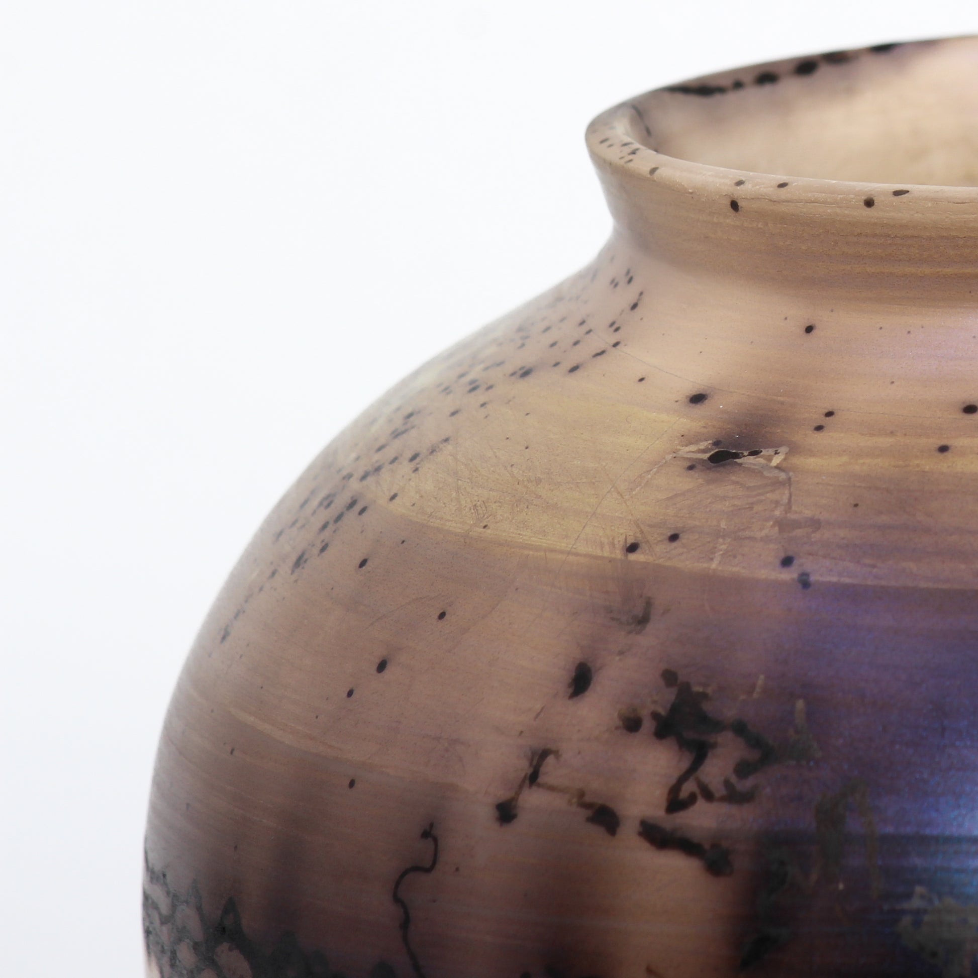 A round ceramic vessel. Surface features black and brown lines from burnt horsehair, with dark brown splotches on a beige surface.