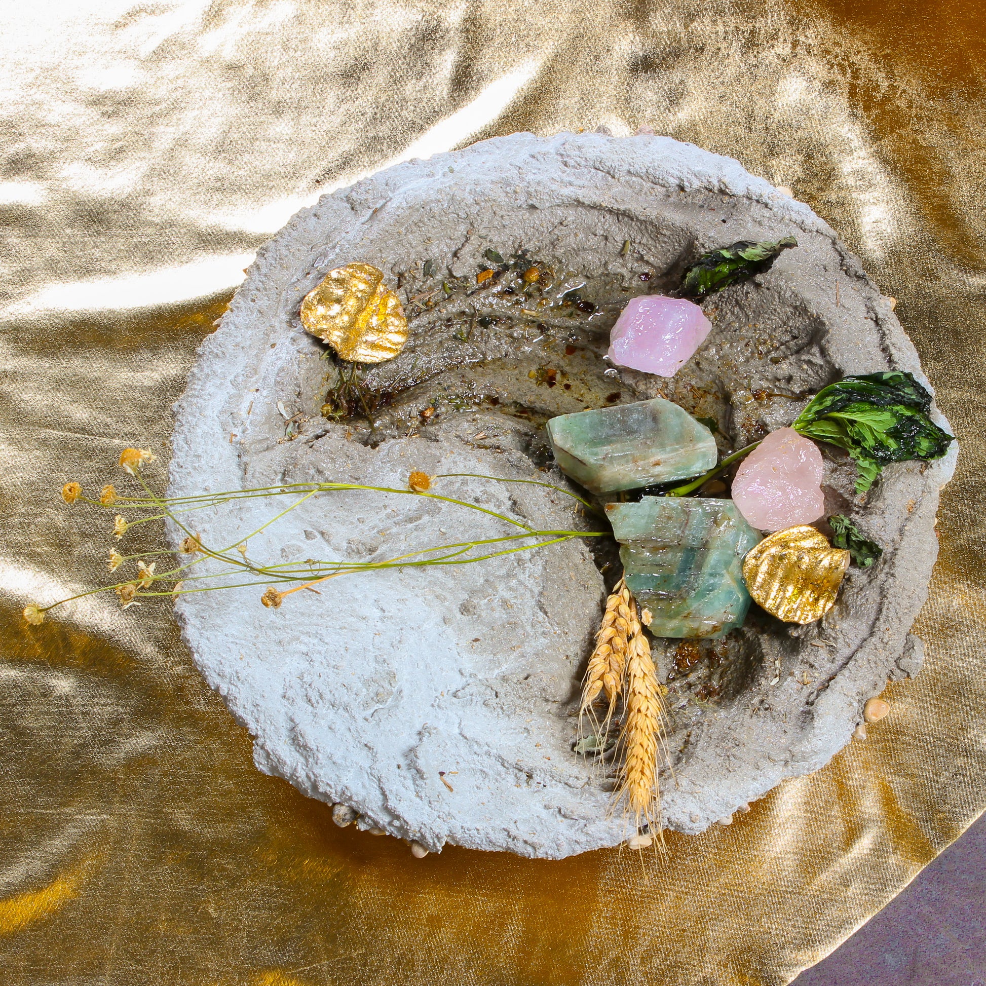 A close up shot of one of the bowl shaped objects. It is made of cement, with crystals, pieces of plant life, and gold chips sitting inside.