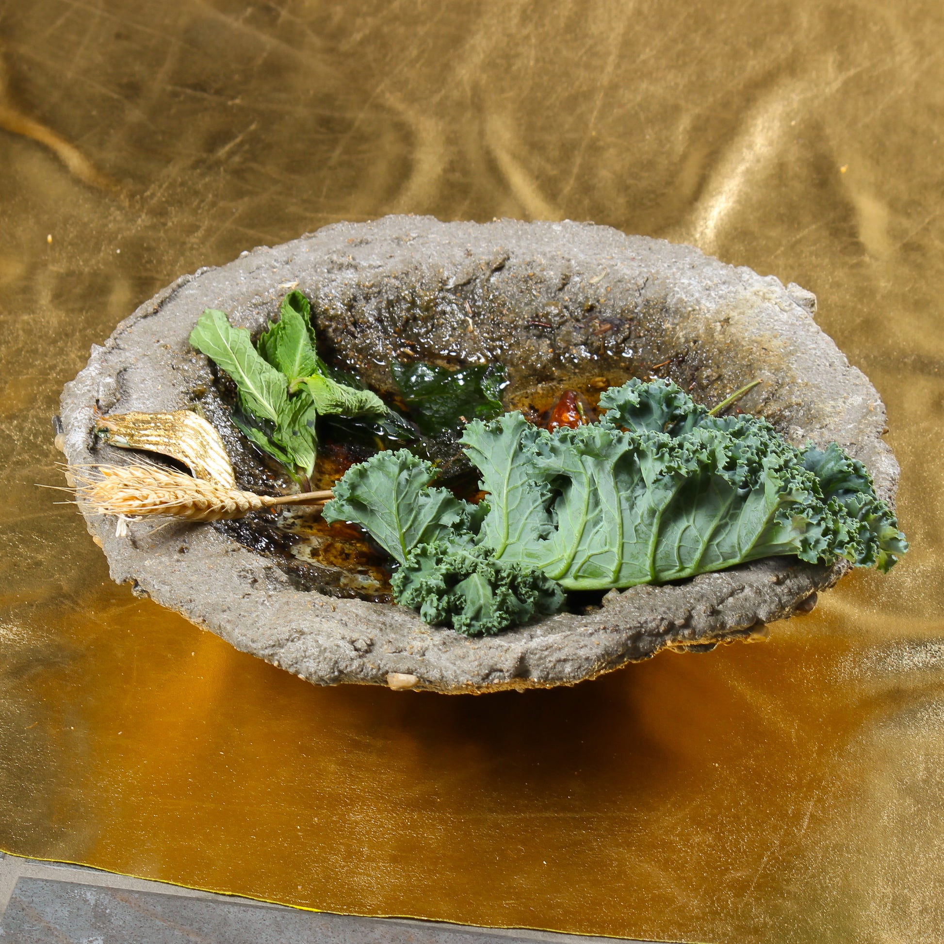 A close up shot of one of the bowl shaped objects. It is made of cement, with pieces of plant life and epoxy that looks like water sitting inside.