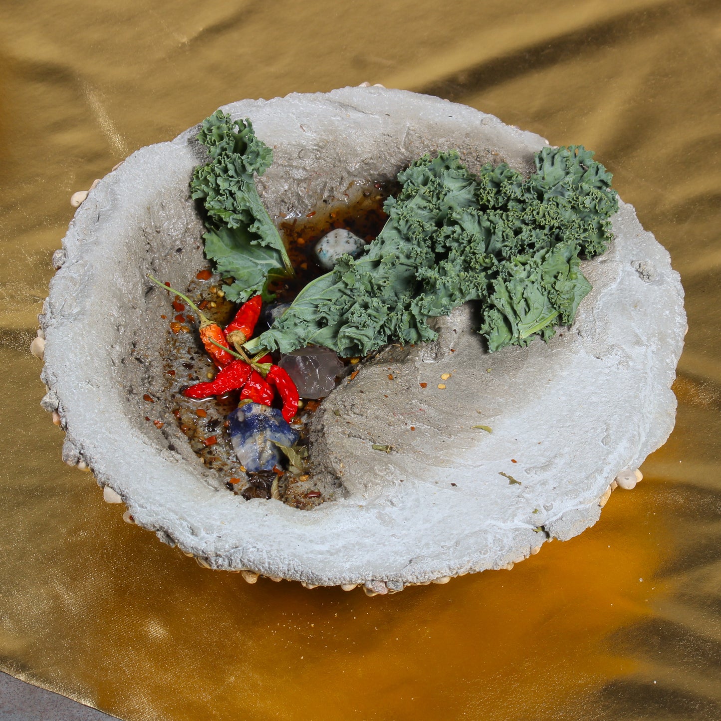 A close up shot of one of the bowl shaped objects. It is made of cement, with tiny hot peppers, pieces of plant life, and epoxy that looks like water sitting inside.