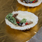 A close up shot of one of the bowl shaped objects. It is made of cement, with tiny hot peppers, pieces of plant life, crystals, and epoxy that looks like water sitting inside.