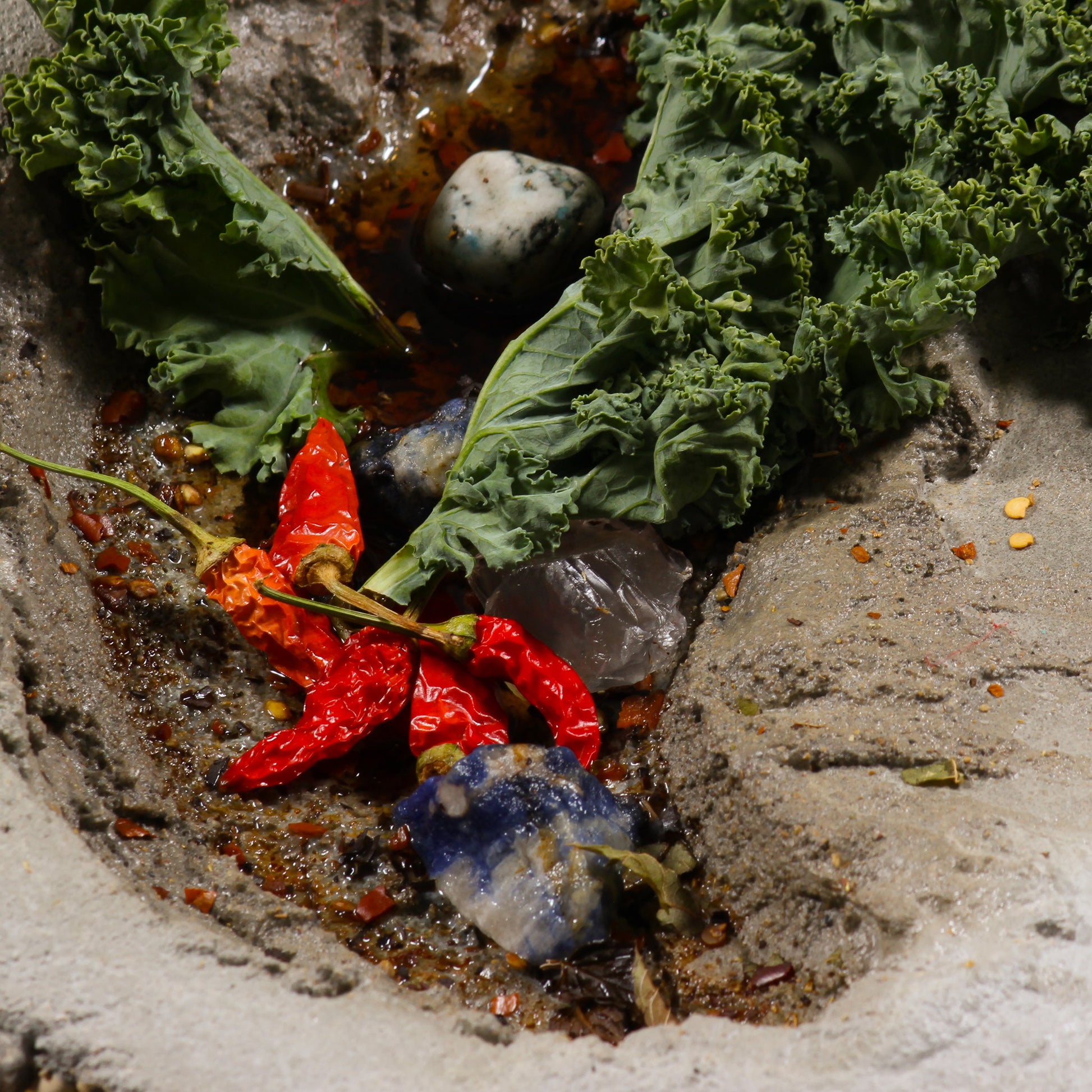 A close up shot of one of the bowl shaped objects, zoomed in on 5 tiny hot peppers, pieces of plant life, stones, and epoxy that looks like water sitting inside.