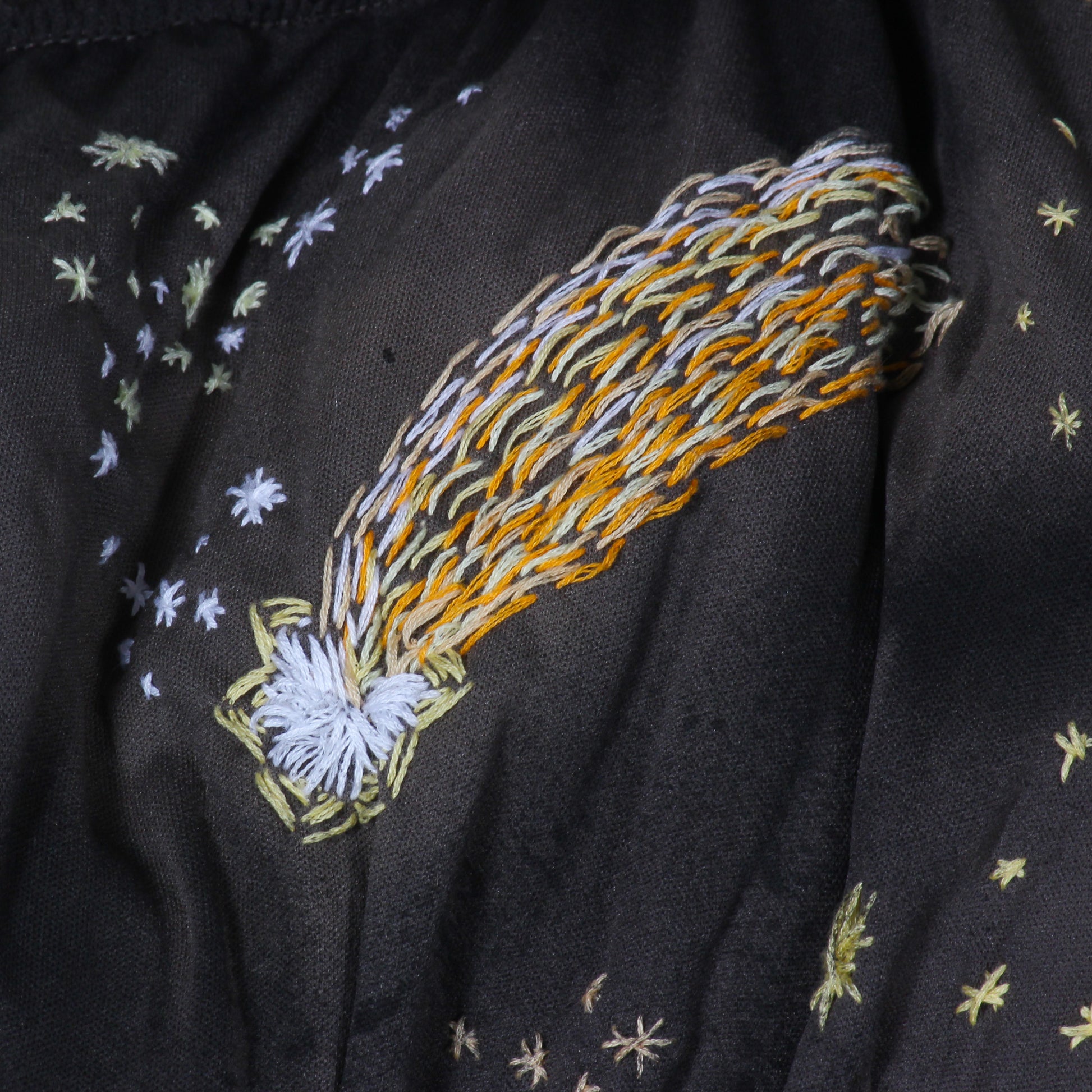 A close up photo of a shooting star embroidered in yellow and white on navy fabric.