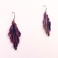 A pair of handmade dangle earrings with textured, pleated leaf-like shapes in a deep purple and burgundy color, suspended from silver fishhook wires against a plain white background.