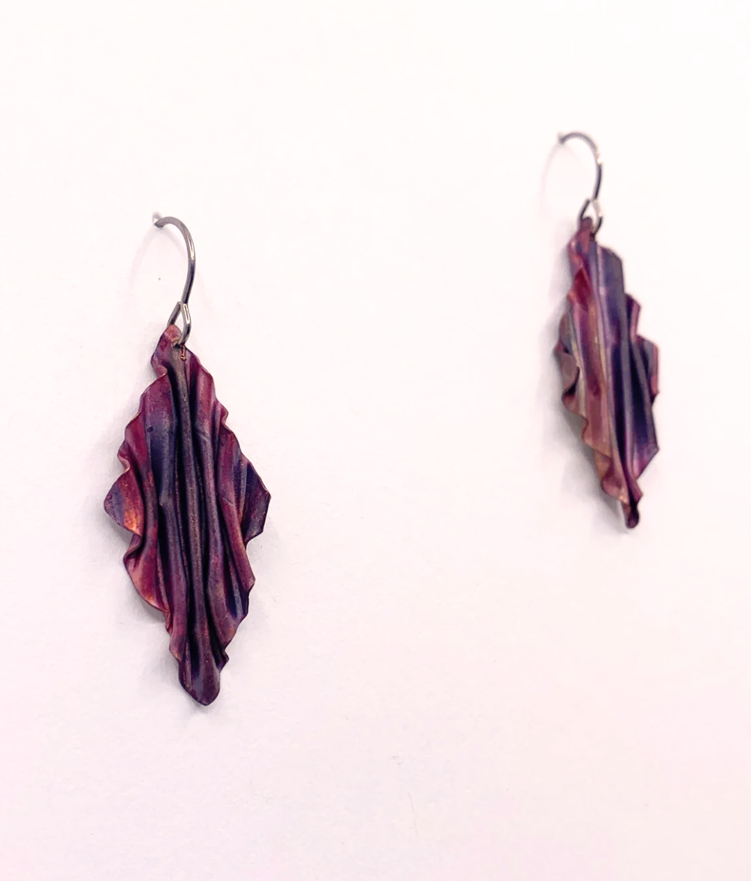 A pair of handmade dangle earrings with textured, pleated leaf-like shapes in a deep purple and burgundy color, suspended from silver fishhook wires against a plain white background.