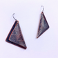 A pair of triangular drop earrings with a dark bronze and copper patinated metal finish, featuring a textured wavy pattern and silver-toned fishhook ear wires, shown on a plain white background.