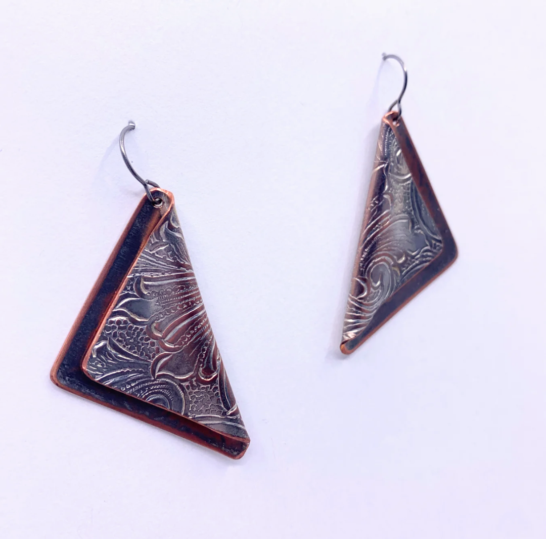A pair of triangular drop earrings with a dark bronze and copper patinated metal finish, featuring a textured wavy pattern and silver-toned fishhook ear wires, shown on a plain white background.