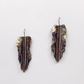 A pair of handmade textured metal earrings shaped like stylized leaves with a central vertical ridge, featuring a mix of bronze, brown, and gold tones, shown against a plain white background.