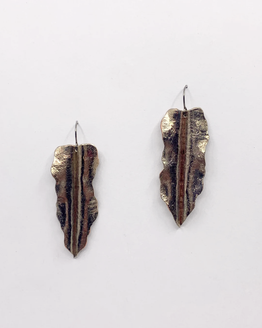 A pair of handmade textured metal earrings shaped like stylized leaves with a central vertical ridge, featuring a mix of bronze, brown, and gold tones, shown against a plain white background.