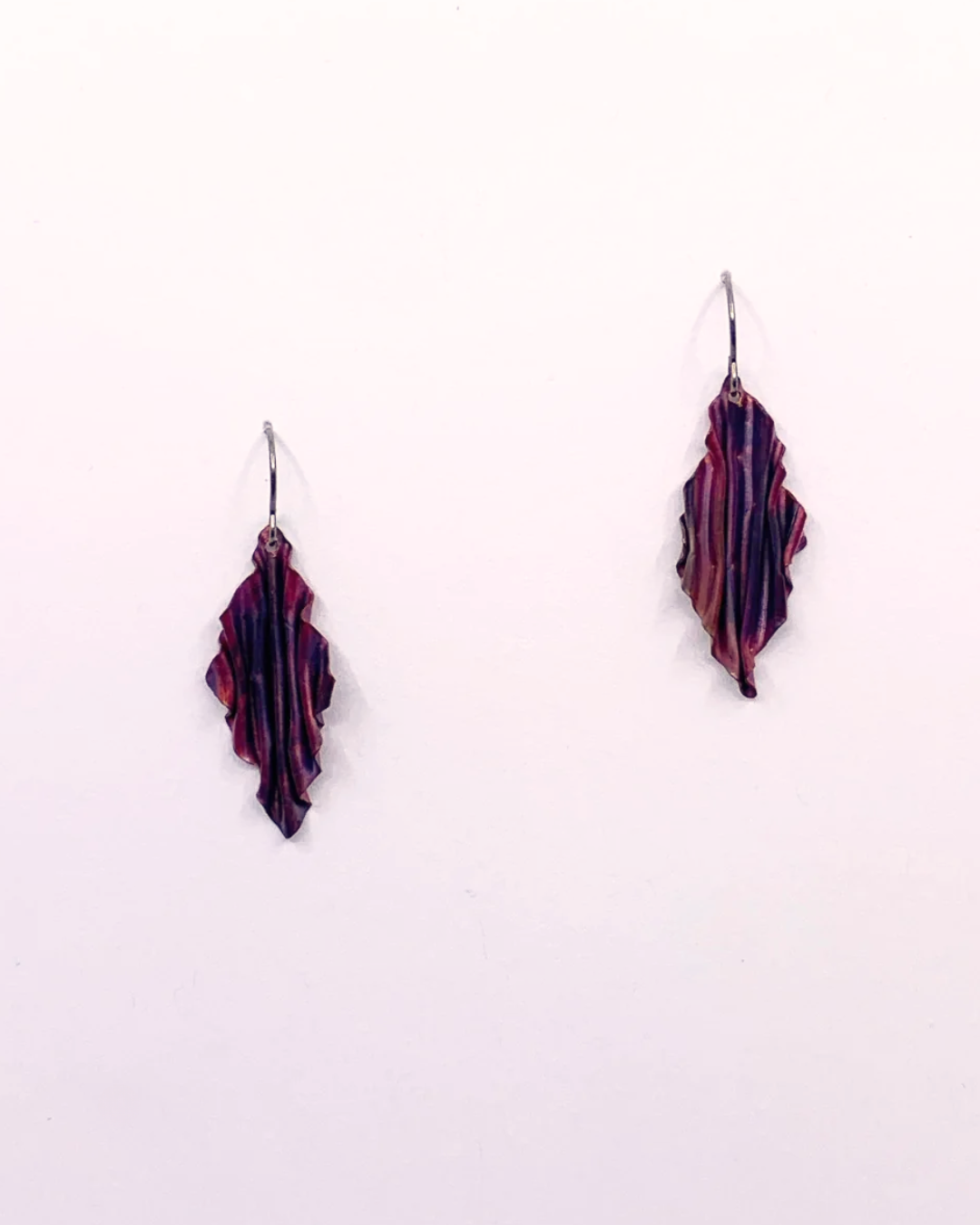 A pair of handmade dangle earrings with a marbled pattern of purple, copper, and black, suspended from silver fishhook wires against a plain white background.