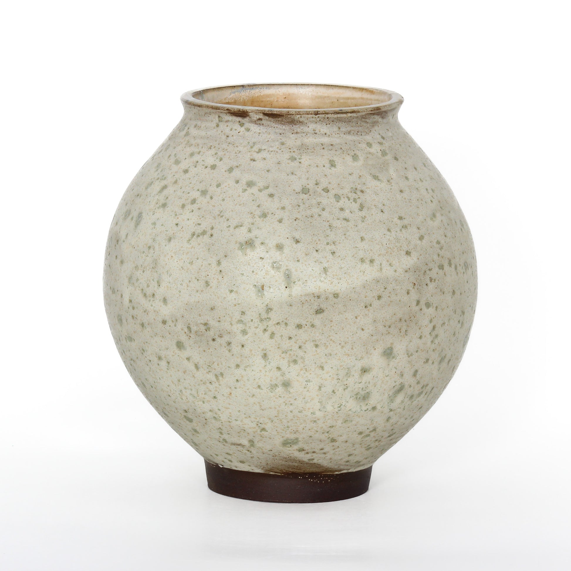 A round ceramic vessel. Glaze is beige with darker tan splotches and a dark brown base.