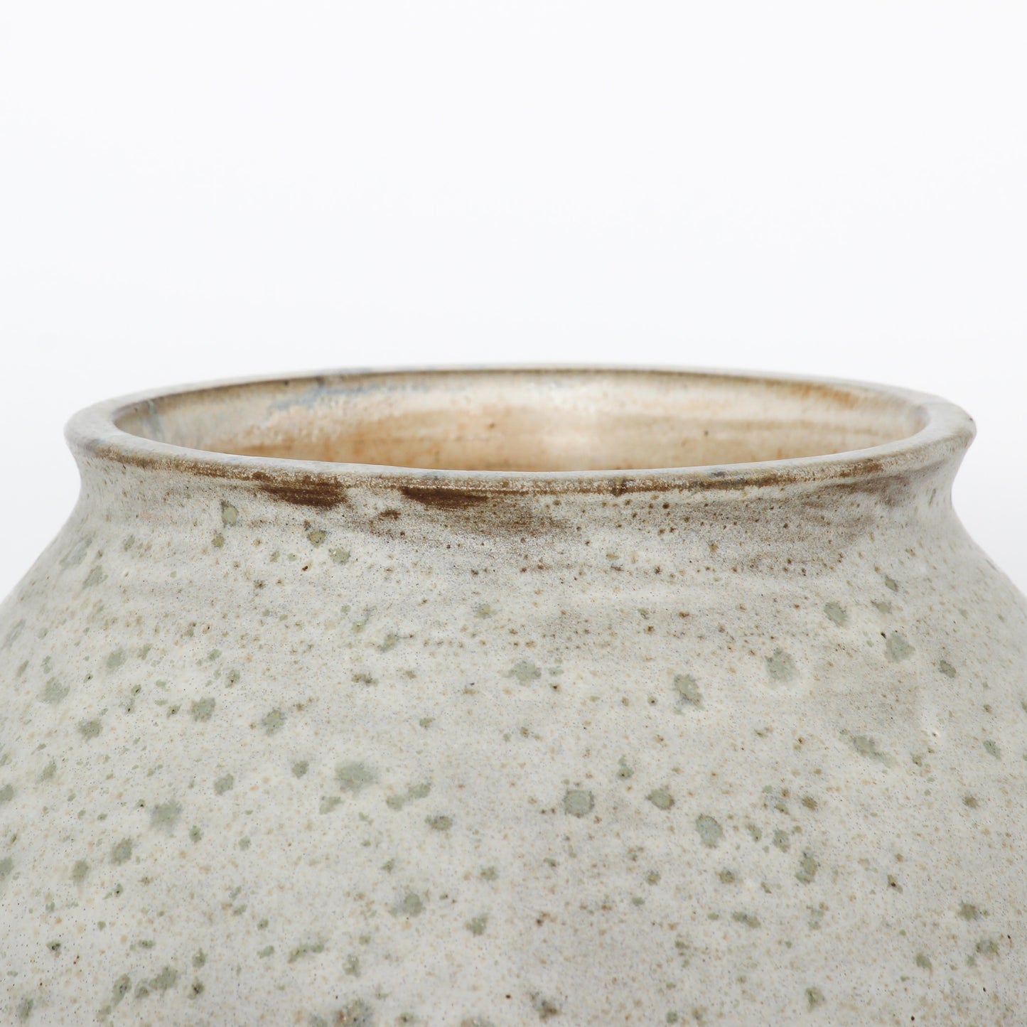 Close up shot of a round ceramic vessel. The mouth is smooth and symmetrical, with textured beige and brown glaze on the outside.