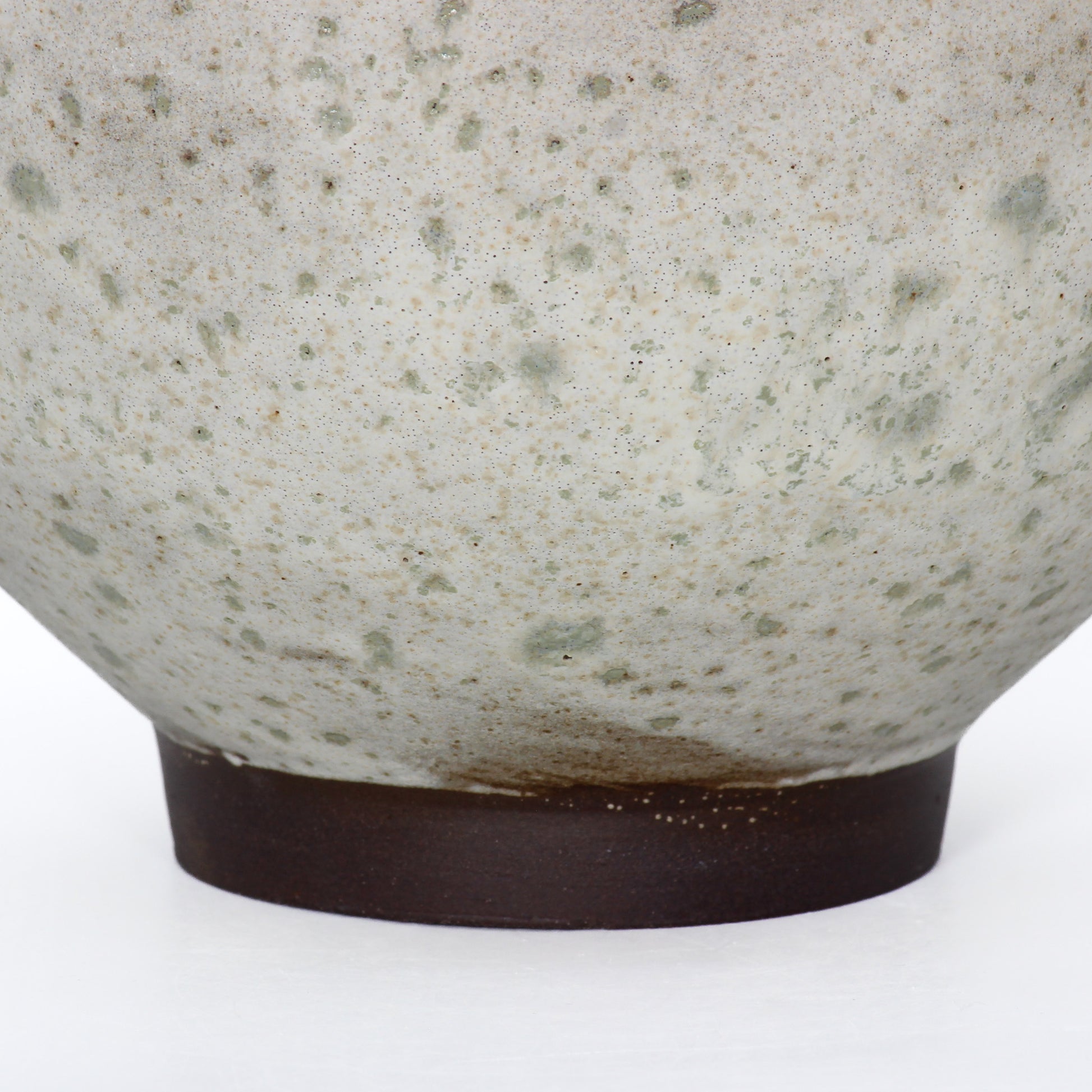 Close up shot of a round ceramic vessel. The base is smooth and symmetrical, with dark brown glaze.