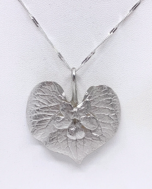 A silver heart-shaped pendant necklace with a textured, leaf-like surface and a small central floral detail, suspended from a twisted silver chain against a white background.