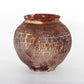 A round ceramic vessel. Glaze is rust, brown, and tan with a crackly texture.