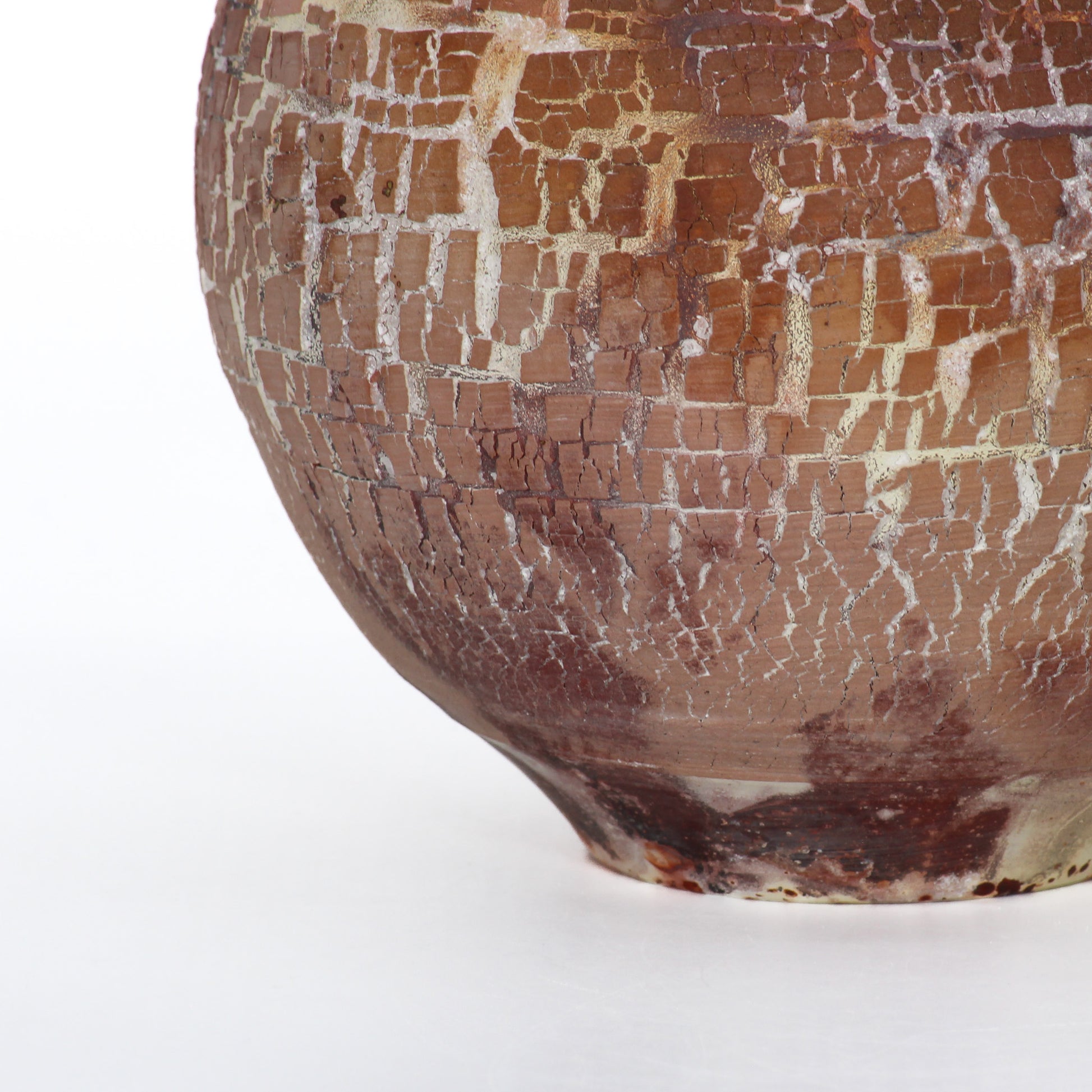 Close up shot of a round ceramic vessel. The base is smooth and symmetrical, with rust brown crackly texture.