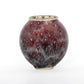 A round ceramic vessel. Glaze is textured, with spots of burgundy and pale blue.