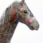 A close-up of a sculpted horse head made from recycled newspaper, featuring printed text and red painted accents, set against a plain white background.